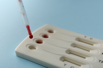 Dropping blood sample onto disposable multi-infection express test cassette with pipette on light...