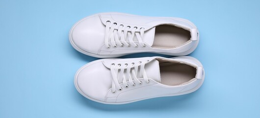 Pair of stylish white sneakers on light blue background, top view