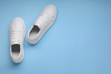 Pair of stylish white sneakers on light blue background, top view. Space for text