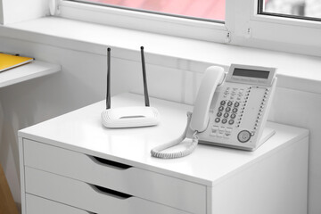 Modern wi-fi router with telephone on shelf in office