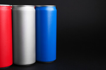Energy drinks in colorful cans on black background, space for text