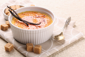 Delicious creme brulee in bowl, vanilla pods, sugar cubes and spoon on light textured table, closeup
