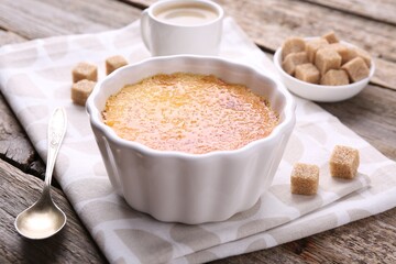 Delicious creme brulee in bowl, sugar cubes and spoon on wooden table, closeup