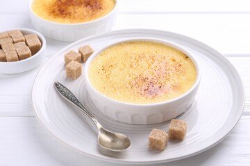 Delicious creme brulee in bowls, sugar cubes and spoon on white wooden table