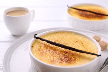 Delicious creme brulee in bowls, vanilla pods, sugar cubes and coffee on white wooden table, closeup