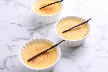 Delicious creme brulee in bowls and vanilla pods on white marble table