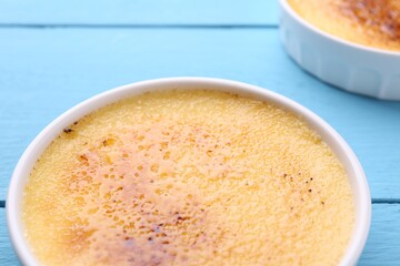 Delicious creme brulee in bowl on light blue wooden table, closeup