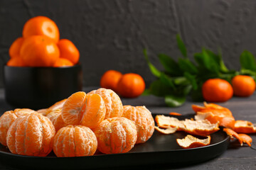 Plate with peeled tangerines on black wooden table