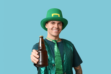 Happy young tattooed man in green clothes and with bottle of beer on blue background. St. Patrick's Day