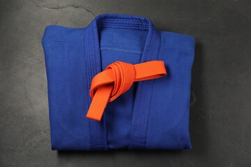 Orange karate belt and blue kimono on gray background, top view