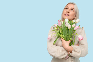 Mature woman with bouquet of beautiful tulips on blue background. International Women's Day