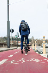 vertical portrait from behind Businessman with backpack on electric folding bike along red bike lane