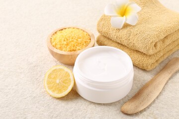 Obraz na płótnie Canvas Body care. Composition with moisturizing cream in open jar and half of lemon on light textured table, closeup
