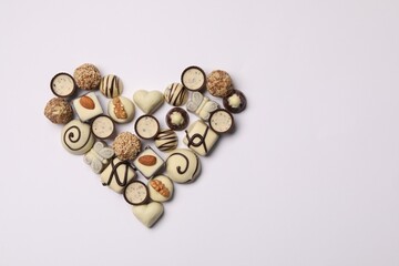 Heart made with delicious chocolate candies on white background, top view