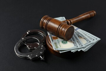 Judge's gavel, money and handcuffs on black background
