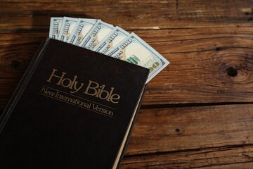 Holy Bible and money on wooden table, closeup. Space for text