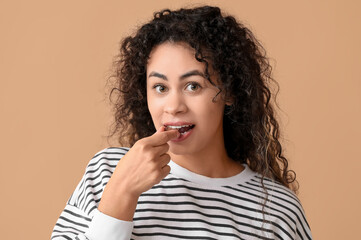 Fototapeta na wymiar Beautiful young African-American woman eating sweet chocolate candy on brown background