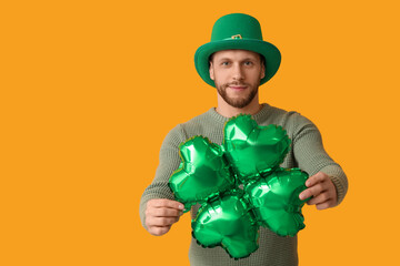 Young man in leprechaun hat with air balloon in shape of clover on yellow background. St. Patrick's...
