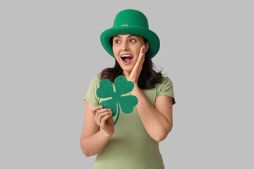Shocked young woman in leprechaun hat with clover on grey background. St. Patrick's Day celebration