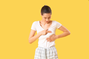 Young woman checking her breast on yellow background. Cancer awareness concept