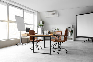Interior of light conference hall with screen board, table and armchairs