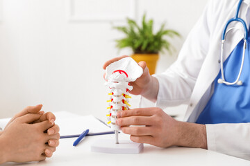 Male doctor explaining spinal anatomy with vertebral column model to patient in clinic, closeup