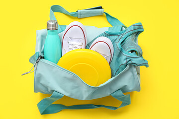 Sports bag with sportswear and workout equipment on yellow background