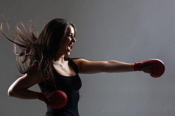 beautiful girl exercising karate punch and screaming  with hair in the air against gray background