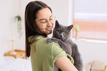 Happy young woman with cute British Shorthair cat in bedroom, closeup © Pixel-Shot