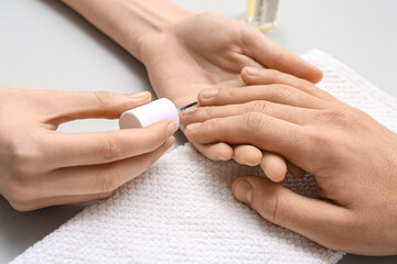 Obraz na płótnie Canvas Manicure master applying cuticle oil onto male fingernails on grey background, closeup