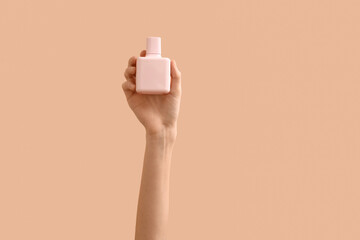 Female hands holding pink perfume bottle on color background