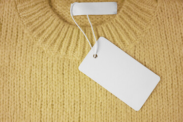 Blank clothing tag and inner label on neck of yellow knitted sweater background. Mockup, template with empty rectangular card for price or text. Shopping, sale, discount, black friday, fashion