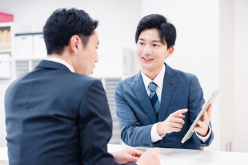 タブレット端末を使い窓口で説明をするビジネスマン