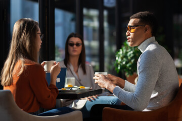 Three friends in a restaurant talking smiling and drinking tea. Business colleagues having a meeting after work or during coffee break at a cafe bar..