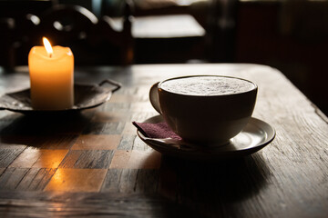 Candle and Cup of coffee latte or cappuccino, plate with napkin and pack of sugar and  lit candles...