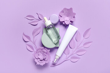 Serum, eye cream, paper flowers and leaves on lilac background