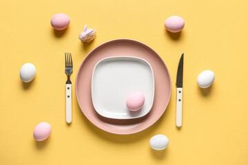 Table setting for Easter celebration with painted eggs on yellow background. Top view