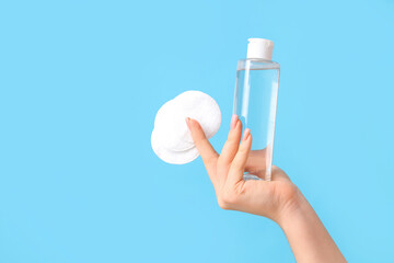 Young woman with micellar water and cotton pads on blue background, closeup
