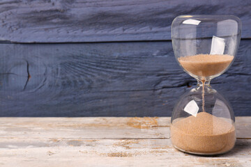 Hourglass on table against blue wooden background. Time management concept