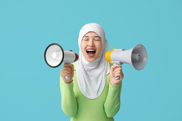 Young Asian Muslim woman shouting into megaphones on blue background. National Be Heard Day