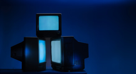 group of vintage televisions with glowing screen on a blue background with free space for text