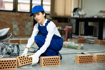 Skilled female builder in blue uniform working inside building under construction, arranging red...