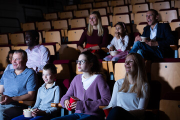 Cheerful people of different ages and nationalities sitting in movie theater with popcorn and watching comedy