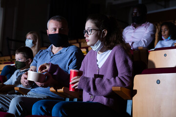 Father with his teenage daughter eating popcorn and watching a movie in the cinema