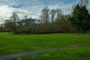 Fototapeta na wymiar 2024-02-20 CONFLUENCE PARK IN ISSAQUAH WITH LUSH GREEN GRASS AND TREES LINING THE SIDE WITH A MOUNTAIN AND BEAUTIFUL SKY IN THE BACKGROUND