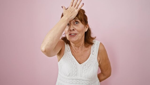 Middle-aged woman in dress, hand on head, realizing a blunder over pink isolated background. oops! forgot again, memory error strikes!