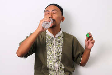 An Indonesian Muslim man in koko and peci breaks his Ramadan fast with a bottle of mineral water at...