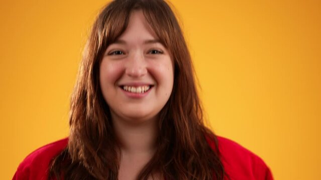 Young happy, laughing woman with brown hair wearing red jacket nodding head yes in agreement gives thumbs up, isolated on yellow background with copy space.