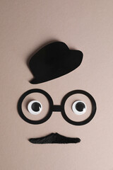 Man's face made of fake mustache, paper hat and glasses on grey background, top view