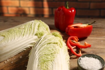 Fresh Chinese cabbages, bell peppers and salt on wooden table, closeup